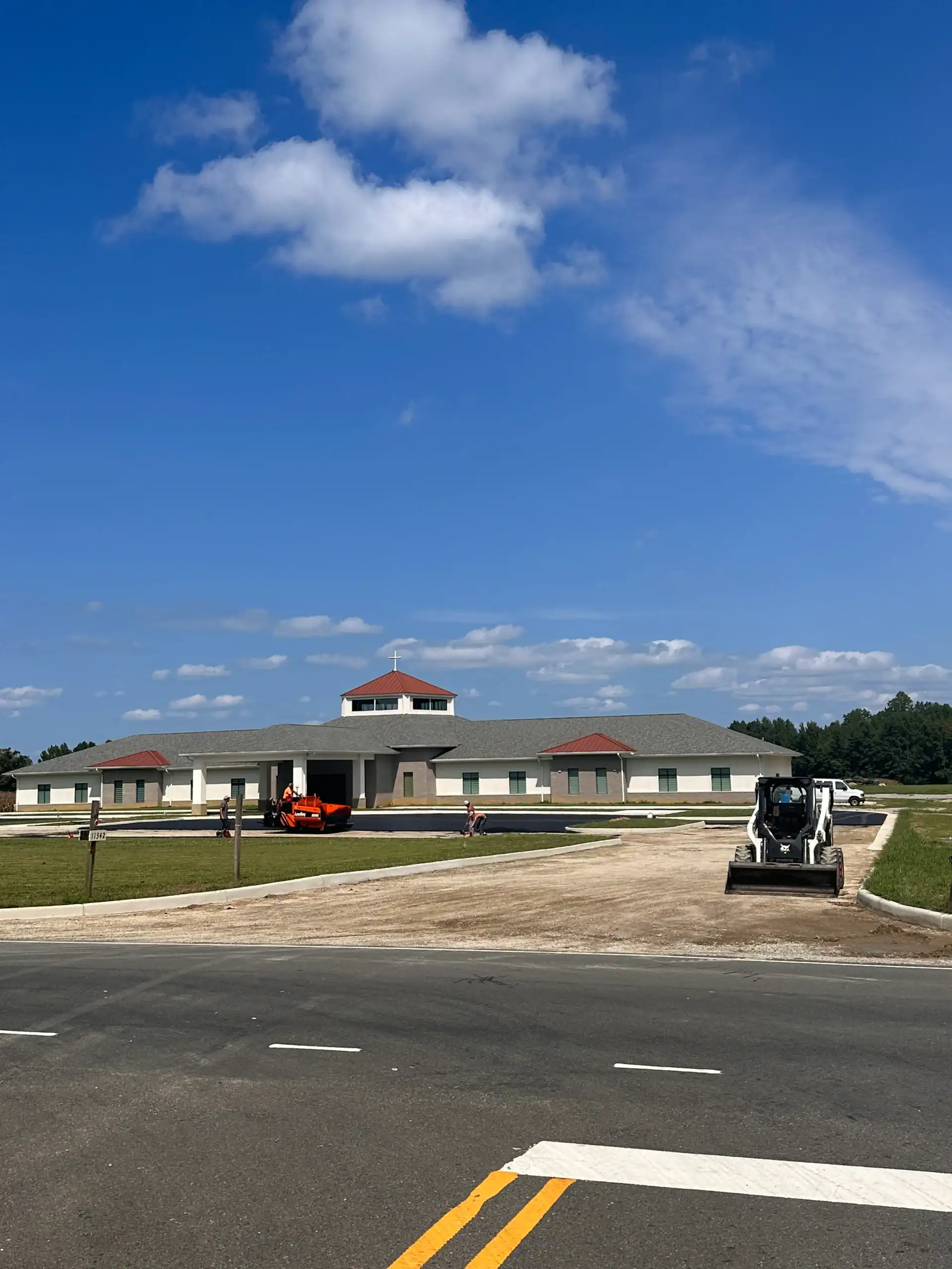 A large building under construction with Maryland and Central and Northern Virginia asphalt paving contractor vehicles onsite, under blue sky.